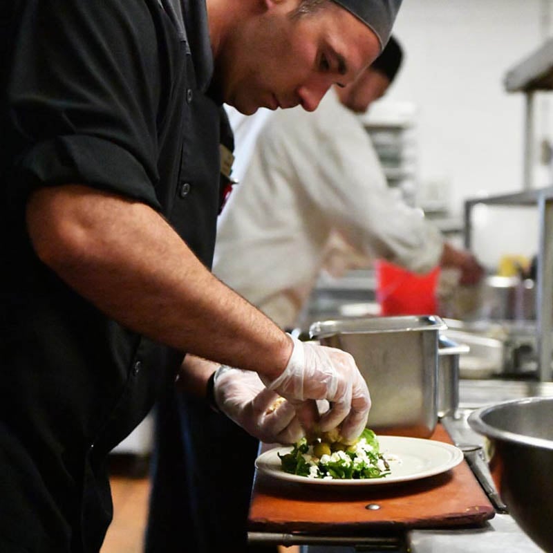 A chef in the kitchen at 10 Wilmington Place plates a saucer of salad