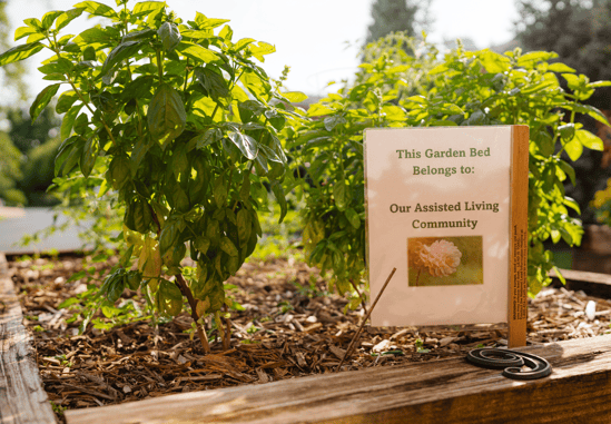 A garden bed with a sign that reads 'This Garden Bed Belongs to: Our Assisted Living Community' is shown.