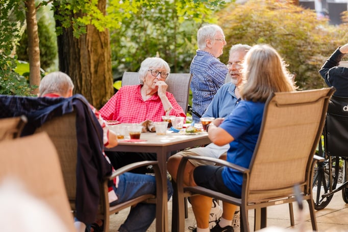 A group of seniors sits around a patio table enjoying food and drinks together.