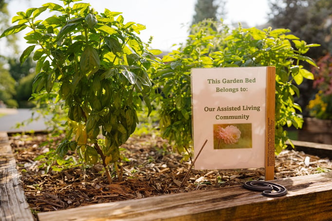 A garden bed is shown with a sign that reads "This Garden Bed Belongs to: Our Assisted Living Community'