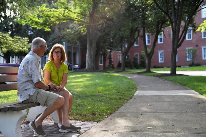 A senior couple sits on a bench in front of 10 Wilmington Place smiling at each other on a sunny day